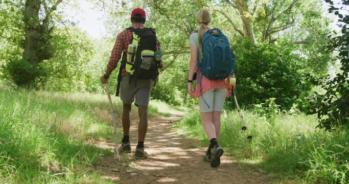 Diverse couple hiking with backpacks in park on sunny day, slow motion