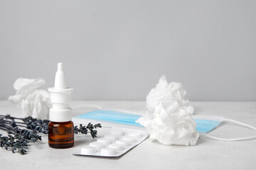 Nasal drops with pills, flowers and tissues on table near grey wall. Seasonal allergy concept