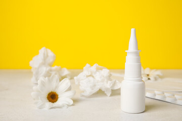 Nasal drops with pills, flowers and tissues on table near yellow wall. Seasonal allergy concept