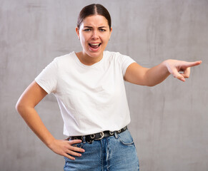 Photo of aggressive young woman banishing crossly standing against light unicoloured background