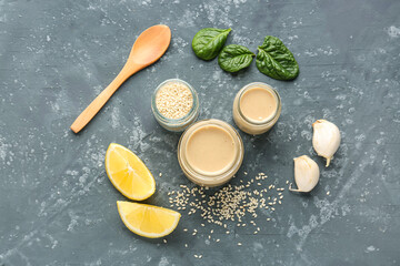 Composition with tasty tahini, sesame seeds, garlic, spinach and lemon slices on dark background - obrazy, fototapety, plakaty