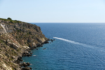 Fototapeta na wymiar a boat goes around a rocky coast in a crystalline sea
