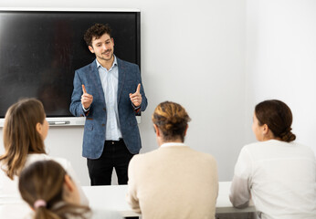 Young male teacher near interactive board, gesturing with hand while consecrating topic of lesson...