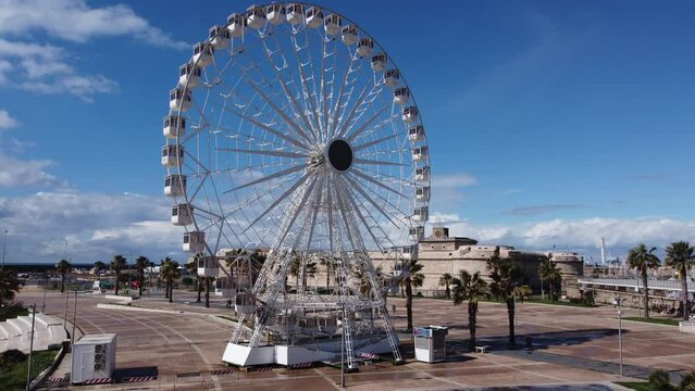 Panoramic view of the city of Civitavecchia with the adjoining tourist port and Forte Michelangelo. Emerald sea and view with tropical palm trees. Ferris wheel and cloudy sky.