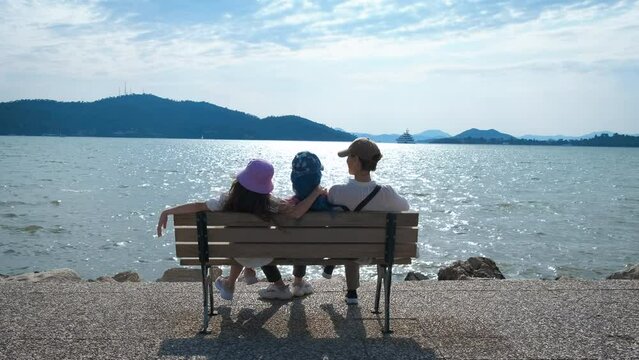 Rest with mom on the bench. Daughters sit with mom on a bench enjoying the seascape.