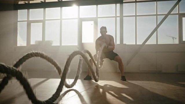 Caucasian young athletic man exercising, battling ropes in an empty urban building. Steadicam shot