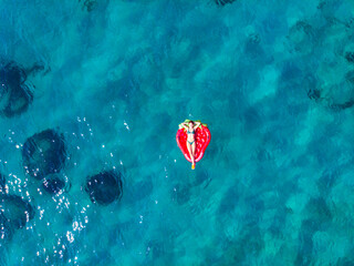 A beautiful girl in a bikini lies and swims on a red strawberry mattress on the turquoise clear water of the Mediterranean Sea. Vacations on the island of Krk, Croatia 