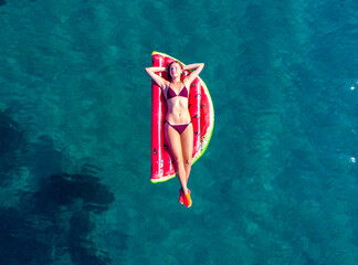 aerial view of beautiful girl in bikini floating on the strawberry shaped mattress in the...