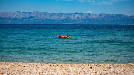relaxed girl in a bikini floating on a strawberry shaped mattress in adriatic sea, croatia; leisure...