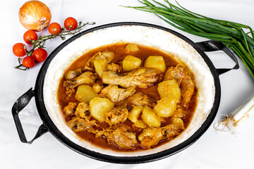 homemade chicken stew with tomato, onion and potato on white fabric table.