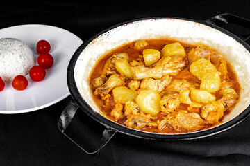 homemade chicken stew with tomato, onion and potato on black fabric table and plate with rice