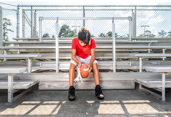 Male youth football player sitting sadly in the stands alone after losing a game