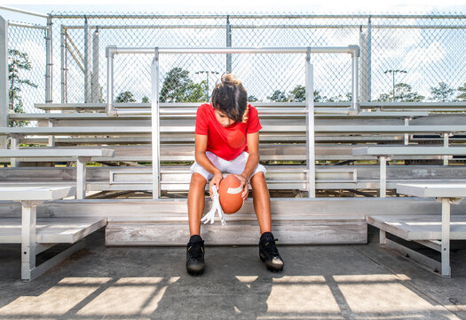 Male youth football player sitting sadly in the stands alone after losing a game