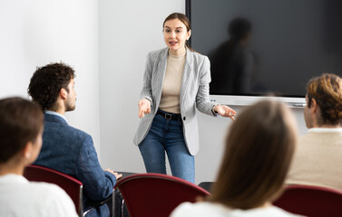 Young woman standing near interactive board and communicating with adult students during advanced...