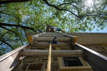Low angle view of man on ladder cleaning gutters of old stone home