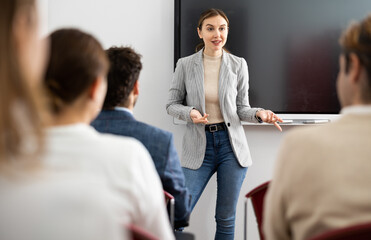 Young female professor explaining subject to classroom full of students