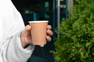 Woman holding cardboard cup of coffee outdoors, closeup. Space for text