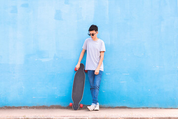 Young man standing at the blue wall with longboard