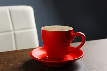 Red cup with cappuccino on wooden table indoors
