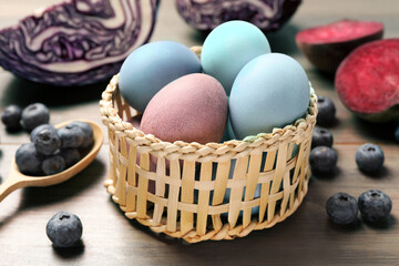 Colorful Easter eggs painted with natural dyes in wicker bowl on wooden table, closeup