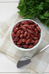 Bowl of canned kidney beans, parsley and spoon on white wooden table, top view