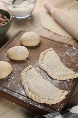 Raw chebureki with tasty filling on wooden table, closeup