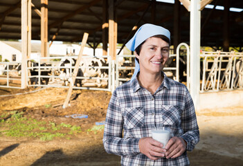 Confident positive french female milker approvingly demonstrating milk on dairy farm