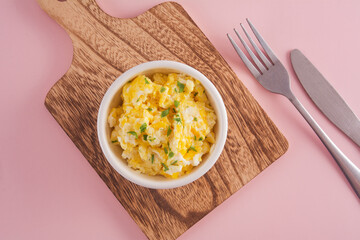Scrambled eggs on bowl, pink background, top view