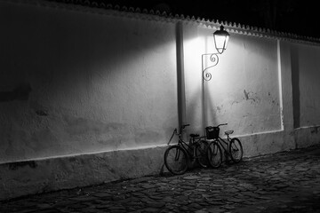 Paraty, Brazil. Bicycles on the wall under the light of old street lamps at night. Street made with stones from the colonial period. Black and white image.