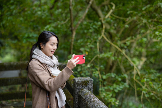 Woman photographing in forest with phone