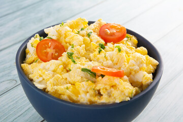 Scrambled eggs with tomatoes on a bowl, wooden table