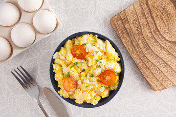 Scrambled eggs with tomatoes on a bowl, white table, top view