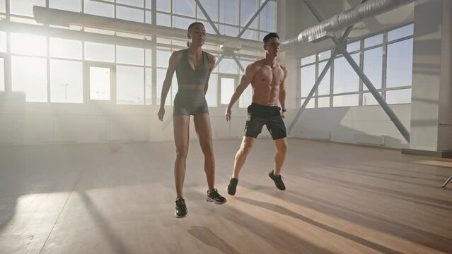 Determined athletic young man and woman doing jumping jack or jumping squats indoors. Slow motion