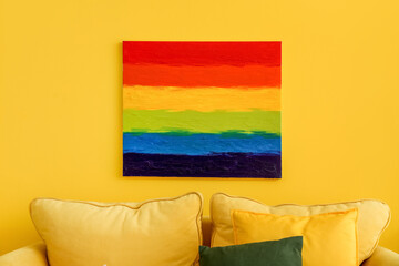 Painting of LGBT flag hanging on yellow wall in living room