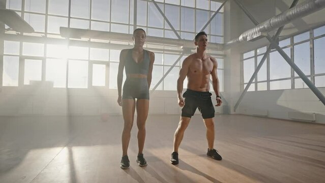 Determined motivated athletic young couple doing jumping jack or jumping squats indoors. Slow motion