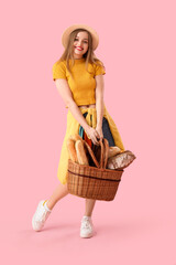Young woman in hat with basket of fresh bread on pink background