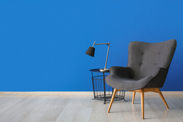 Stylish grey armchair and lamp on end table near blue wall