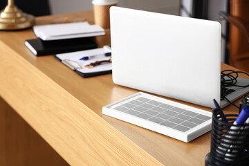 Portable solar panel and laptop on table in office, closeup