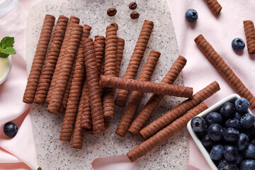 Board with delicious chocolate wafer rolls, blueberries and coffee beans on pink tile background