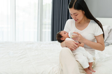 mother feeding milk bottle to her newborn baby on bed