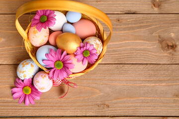 Obraz na płótnie Canvas Wicker basket with painted Easter eggs and chrysanthemum flowers on brown wooden background