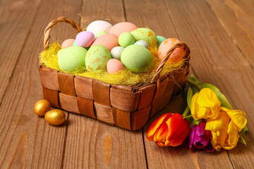 Wicker basket with painted Easter eggs on brown wooden background
