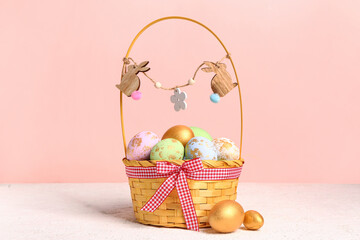 Wicker basket with painted Easter eggs on white table near pink wall