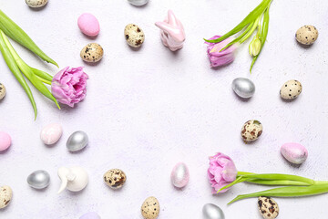 Frame made of Easter quail eggs, bunnies and tulip flowers on white background