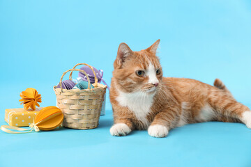 Fototapeta na wymiar Cute cat, basket with Easter eggs and gift on blue background