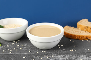 Bowls with tahini and sesame seeds on dark wooden table near color wall