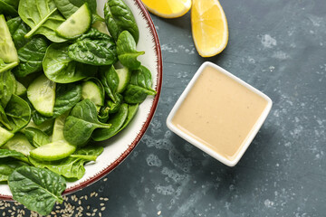 Bowl of tasty salad, tahini, and lemon slices on dark background, closeup