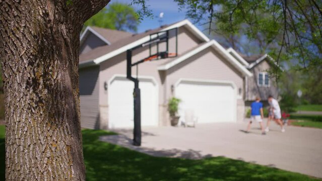 Two Teenage Boys Playing Playing Basketball In Their Driveway On A Blue Sunny Day Out OF Focus