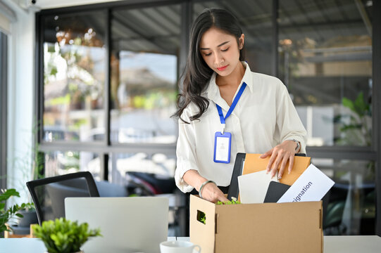 Unhappy Asian female office worker packing her stuff, quitting her job or getting fired from her boss
