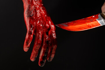 Man holding knife with bloody hand on black background. 